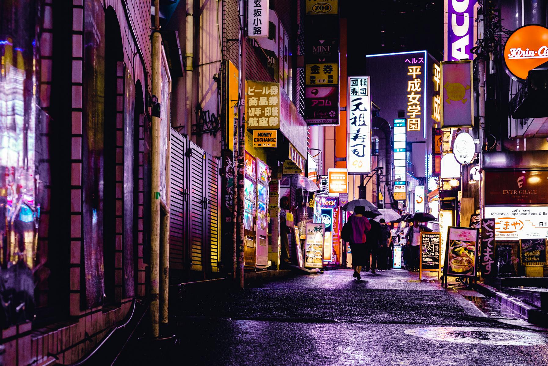 Colorful neon lights illuminate a bustling Tokyo street at night, with reflections on wet pavement.