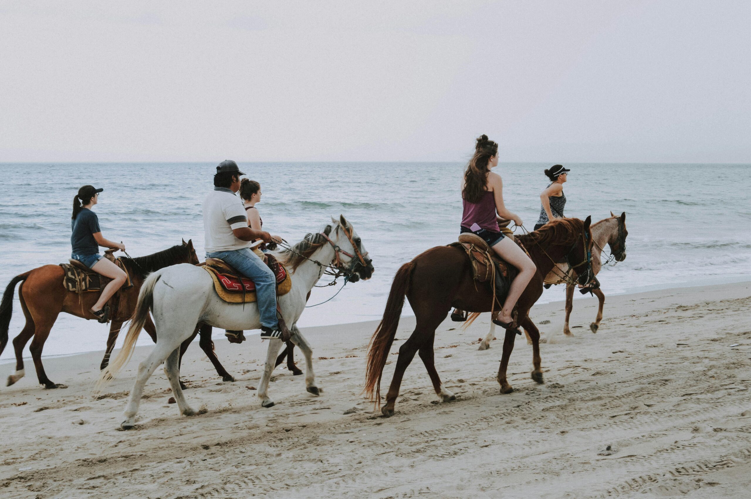 Group of people enjoying horseback riding along Bucerías beach, Mexico, against ocean waves.