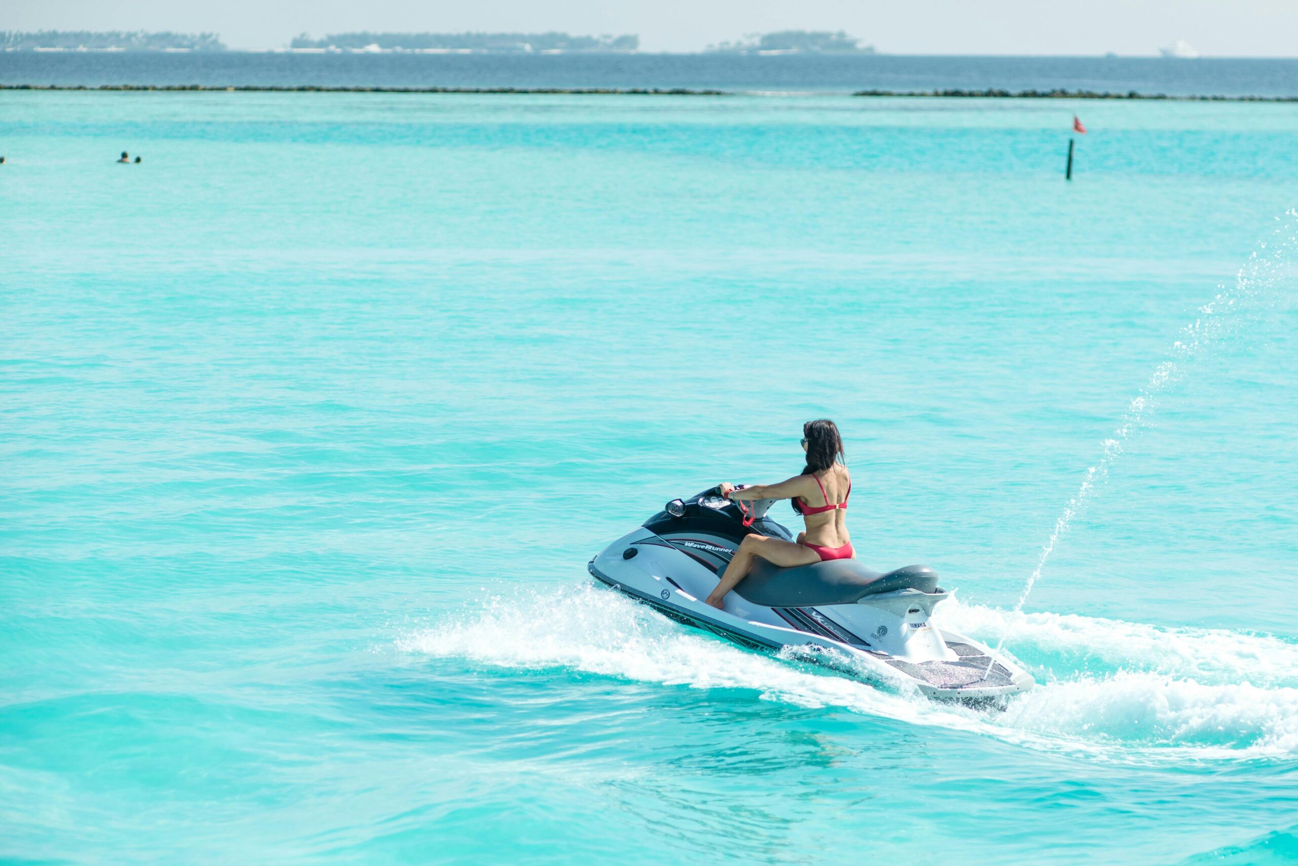 A woman in a bikini rides a jet ski in the turquoise waters of the Maldives, enjoying a sunny day.